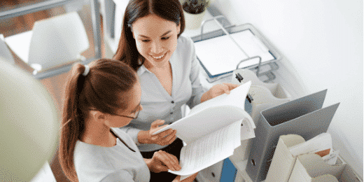 Two women reading papers together and smiling.