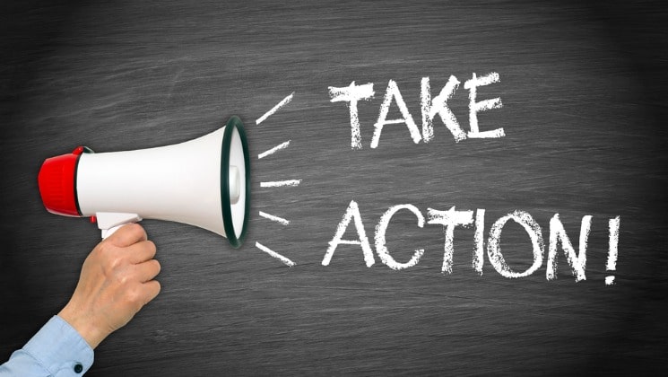 Business man's hand holding a megaphone with the text "take action!" written in chalk on a chalkboard