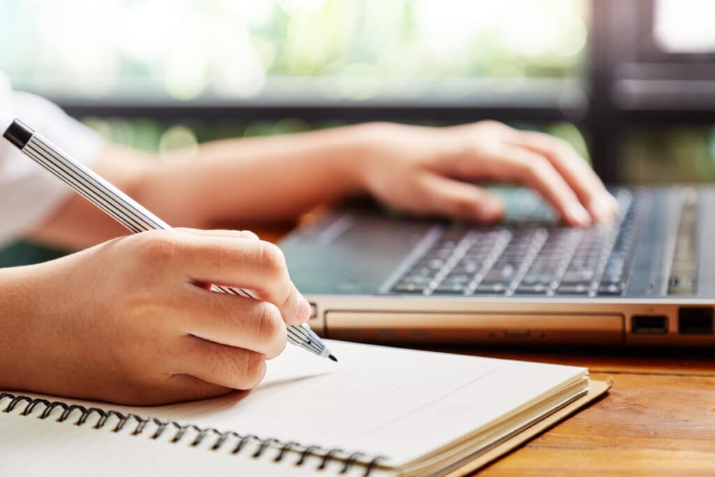 person with hand on laptop and open notebook