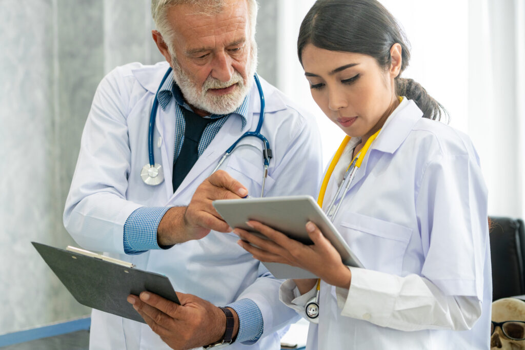 Senior male doctor using tablet computer while discussing with another doctor at the hospital. Medical healthcare staff and doctor service.