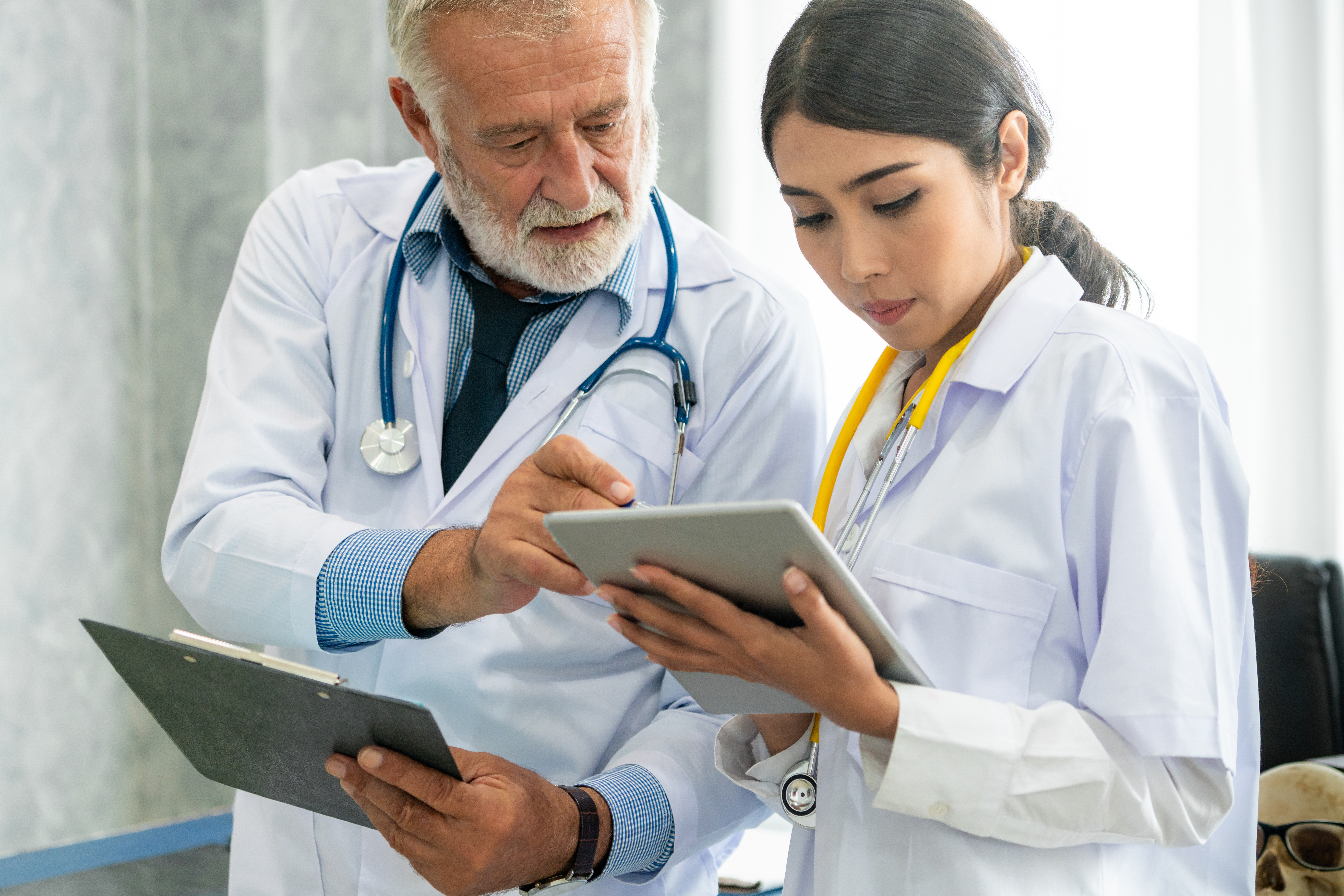 Senior male doctor using tablet computer while discussing with another doctor at the hospital. Medical healthcare staff and doctor service.