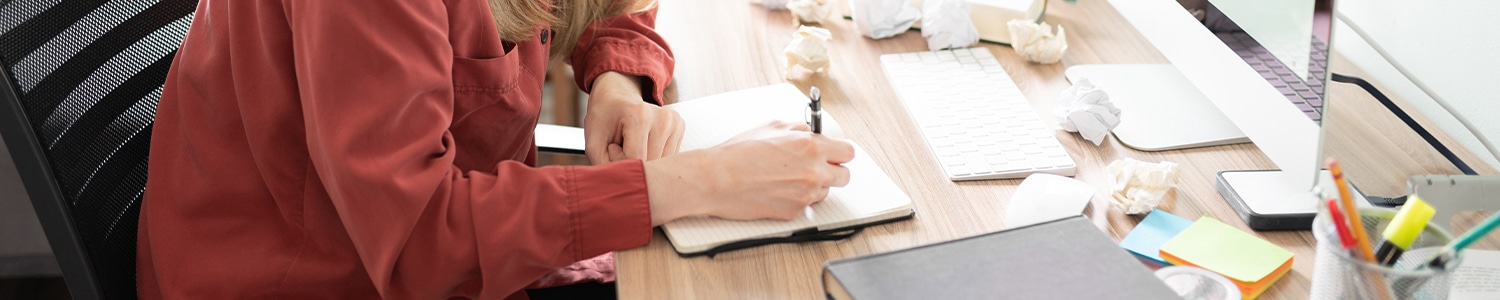 woman writing in notebook with sticky notes on desk