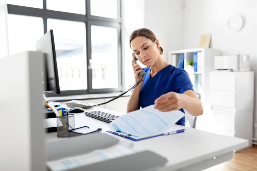 medicine, technology and healthcare concept - female doctor or nurse with computer and clipboard calling on phone at hospital